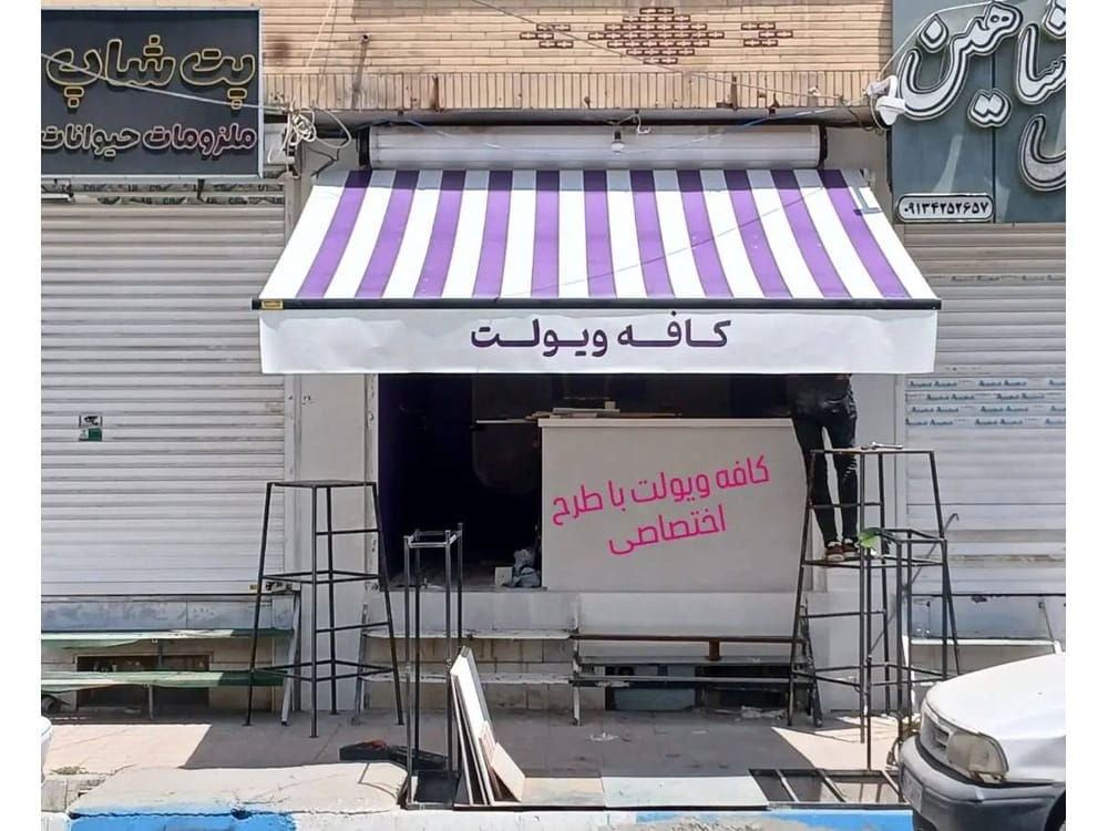 سایبان بازویی راه‌راه بنفش و سفید با نام کافه ویولت روی آویز جلویی در تهران